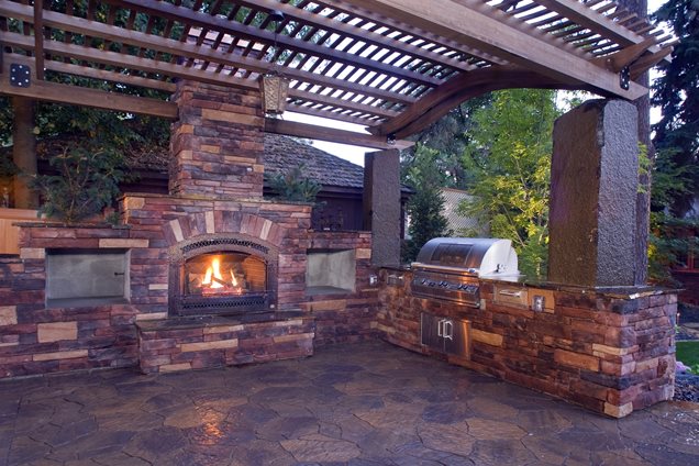 This outdoor kitchen is shaded by a pergola during the day and warmed ...